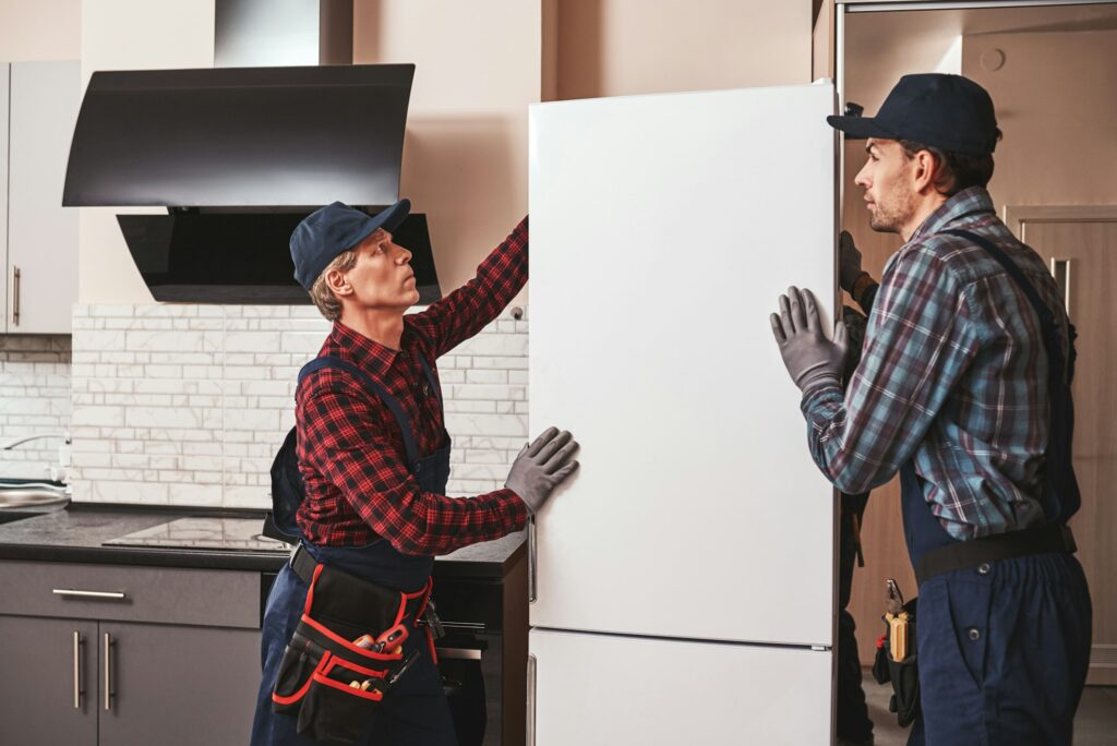 Moving again. Young men mechanics moving refrigerator