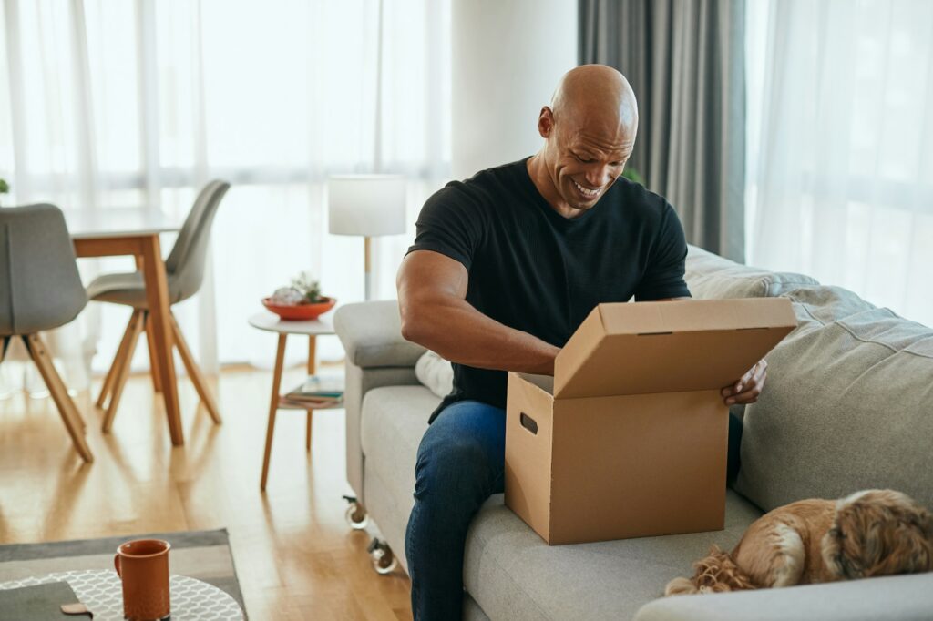 Surprised African American man opening cardboard box at home.